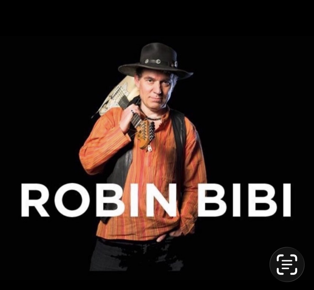 Robin Bibi in a wide-brimmed hat and orange shirt with an electric guitar resting on his shoulder