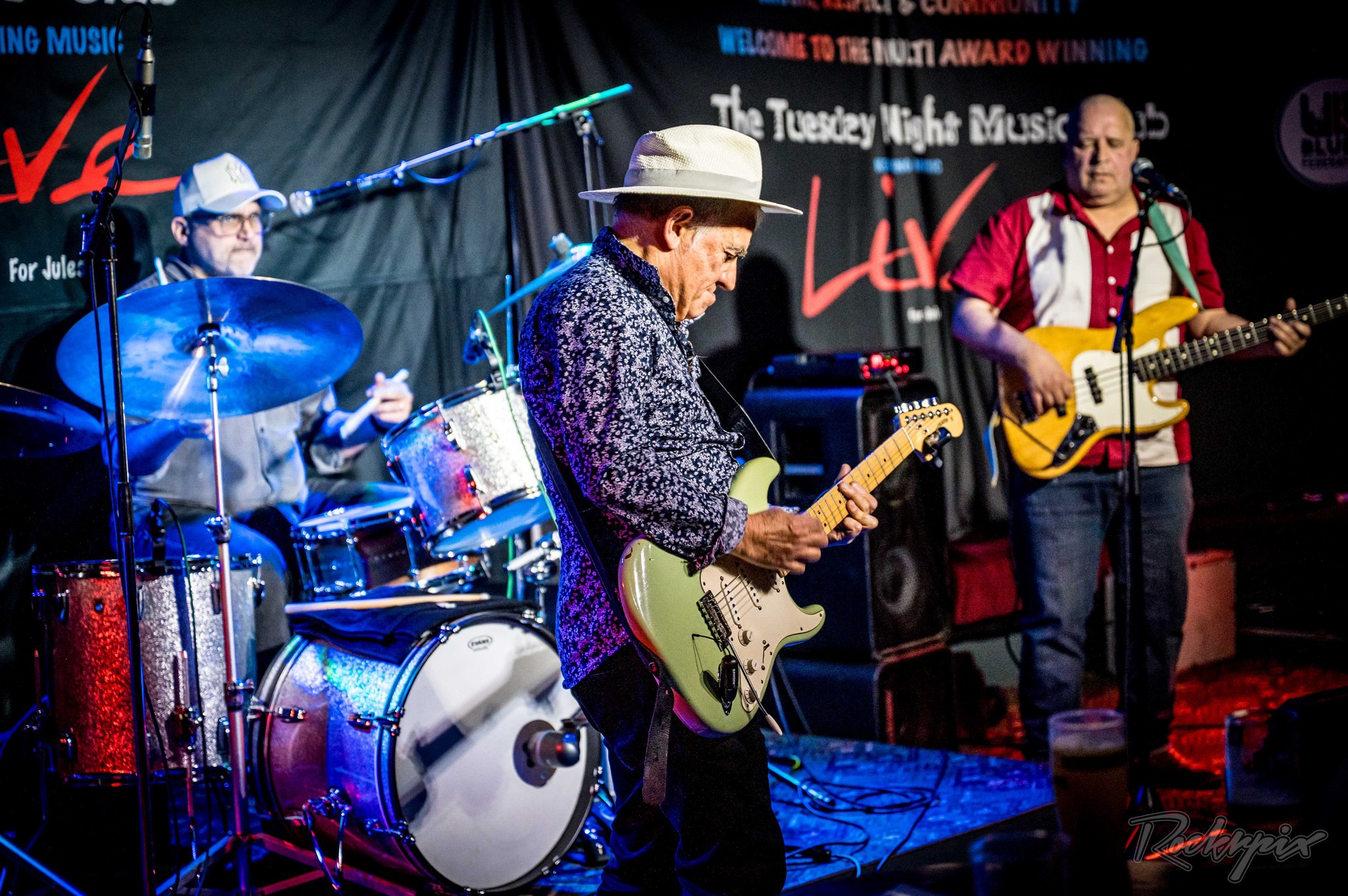 The Robin Bibi Band on stage — drummer behind the kit, Robin on guitar and the bassist mid-song